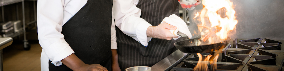 Instructor and Student in the kitchen holding a skillet over an open flame